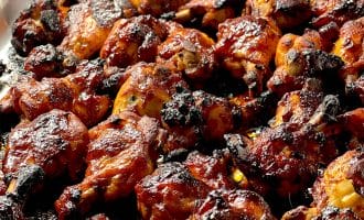 Barbecue chicken wings covered in a glossy, caramelised sauce, slightly charred, arranged closely together on a foil-lined baking tray.