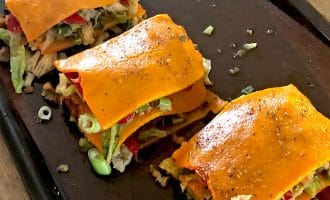 Three servings of vegetable lasagne made with orange squash slices instead of pasta sheets, layered with various vegetables, placed on a dark baking tray.