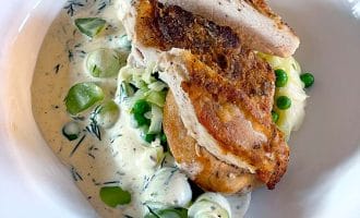 Sliced roasted chicken breast served over creamy pasta with garden peas and courgette, garnished with fresh herbs in a white bowl.