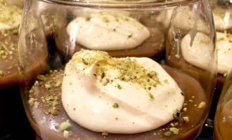 Glasses filled with chocolate mousse, each topped with a dollop of whipped cream and sprinkled with crushed pistachios.