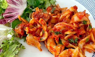 A plate with a portion of marinated seafood salad in red sauce, garnished with herbs, served alongside a mixed green salad with leafy greens.