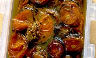 A plastic container filled with slow-roasted tomatoes covered in olive oil, showing shrivelled, glossy red tomato halves and seasoning.