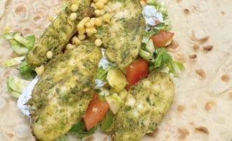 An open flatbread wrap topped with herbed chicken pieces, chopped lettuce, diced tomatoes, sweetcorn kernels, and a white sauce, ready to be folded.