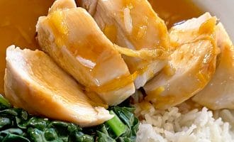 Sliced chicken breast drizzled with brown sauce, served with steamed white rice and leafy cooked greens on a white plate.