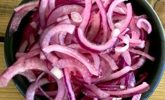 A black bowl filled with thinly sliced red onions, placed on a wooden surface.