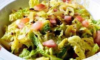A decorative bowl filled with a fresh salad made of chopped leafy greens, caramelised onions, and diced pink vegetables, possibly apples or tomatoes. The salad is lightly tossed and appears crisp and colourful.
