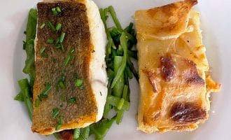 A white plate with a piece of fish with crispy skin and chopped chives, served on green beans, next to a slice of cheesy potato gratin.