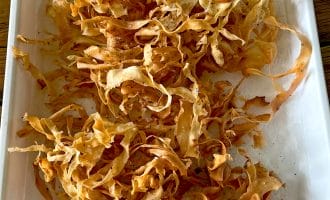 A tray lined with kitchen paper holds a pile of crispy, golden-brown parsnip crisps, freshly cooked and lightly seasoned.