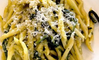 A plate of pasta topped with grated cheese and mixed with green leafy vegetables, served on a white plate.