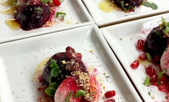 Four rectangular plates each with a vibrant salad of roasted beetroot, creamy cheese, pomegranate seeds, herbs, crushed nuts, and a drizzle of dressing, artfully arranged for serving.