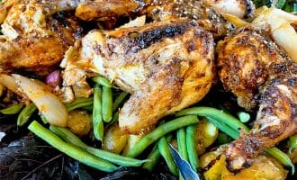 A plate of roast chicken pieces served on a bed of green beans, new potatoes, onions, and leafy greens, garnished with herbs.