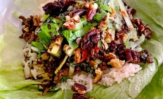 A lettuce leaf filled with white rice, minced meat, chopped spring onions, pecans, and assorted vegetables, served as a wrap.