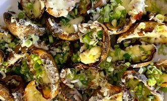 A plate of baked potato skins topped with melted cheese and chopped spring onions, arranged closely together on a white dish.