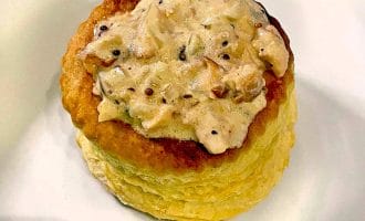 A golden, round puff pastry case filled with a creamy, mushroom and herb sauce, served on a white plate.