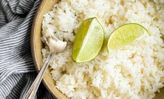 A bowl of white rice topped with two lime wedges, with a silver fork resting at the side. The bowl is placed on a grey and white striped cloth.